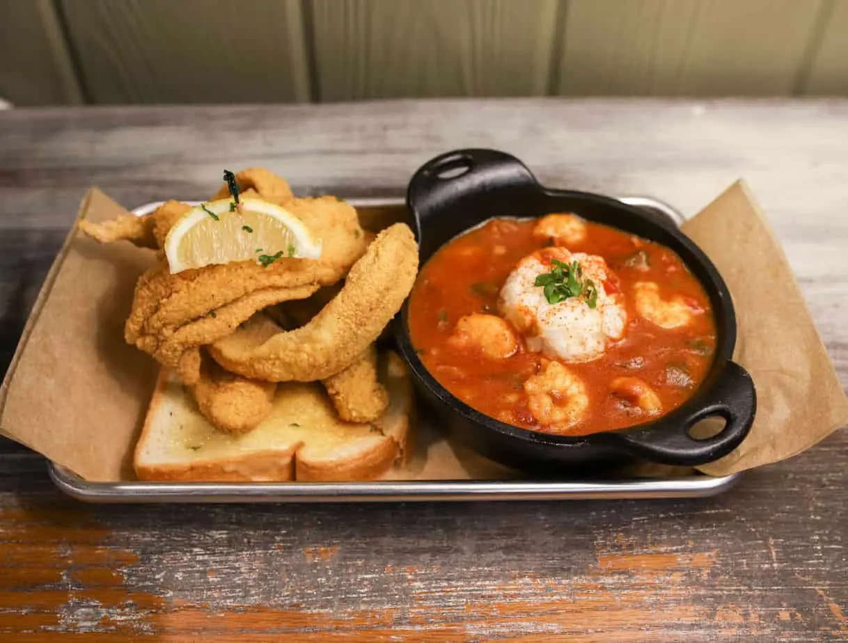 Fried fish on toast with a small cast iron bowl of shrimp in red sauce